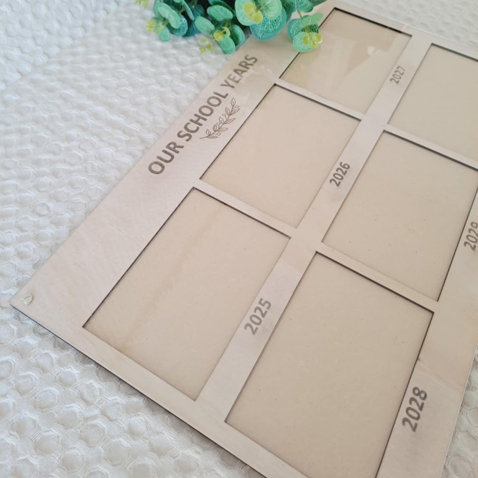 Beige photo board with cut-out years for 2025 to 2028 on a textured surface with greenery.