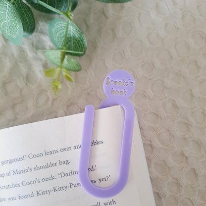 Purple bookmark on a book with a textured surface and green leaves in the background