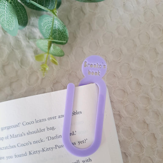 Purple bookmark on a book with a textured surface and green leaves in the background