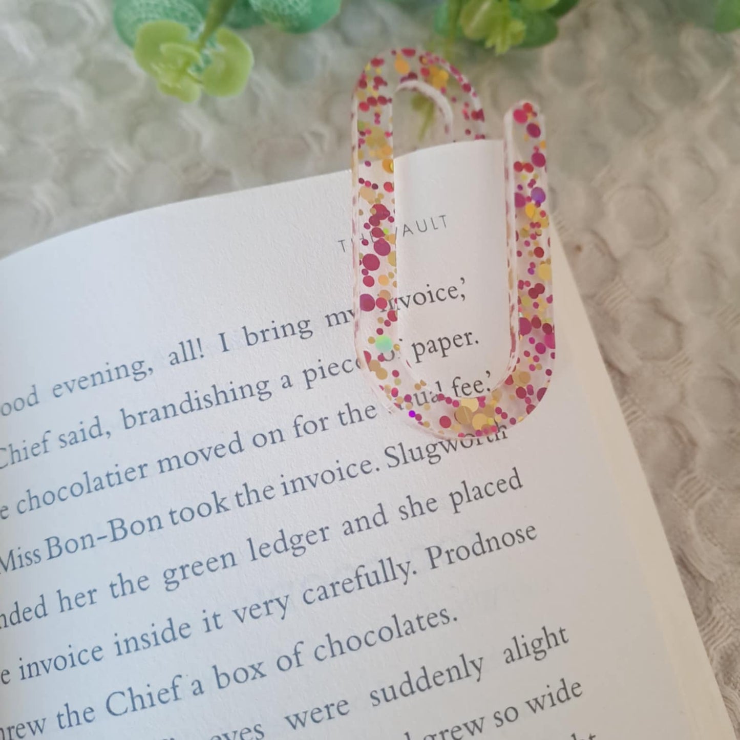 Glitter acrylic jumbo paperclip used as a bookmark in an open notebook.