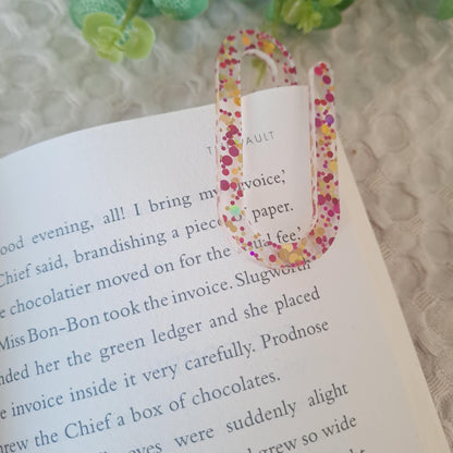 Glitter acrylic jumbo paperclip used as a bookmark in an open notebook.